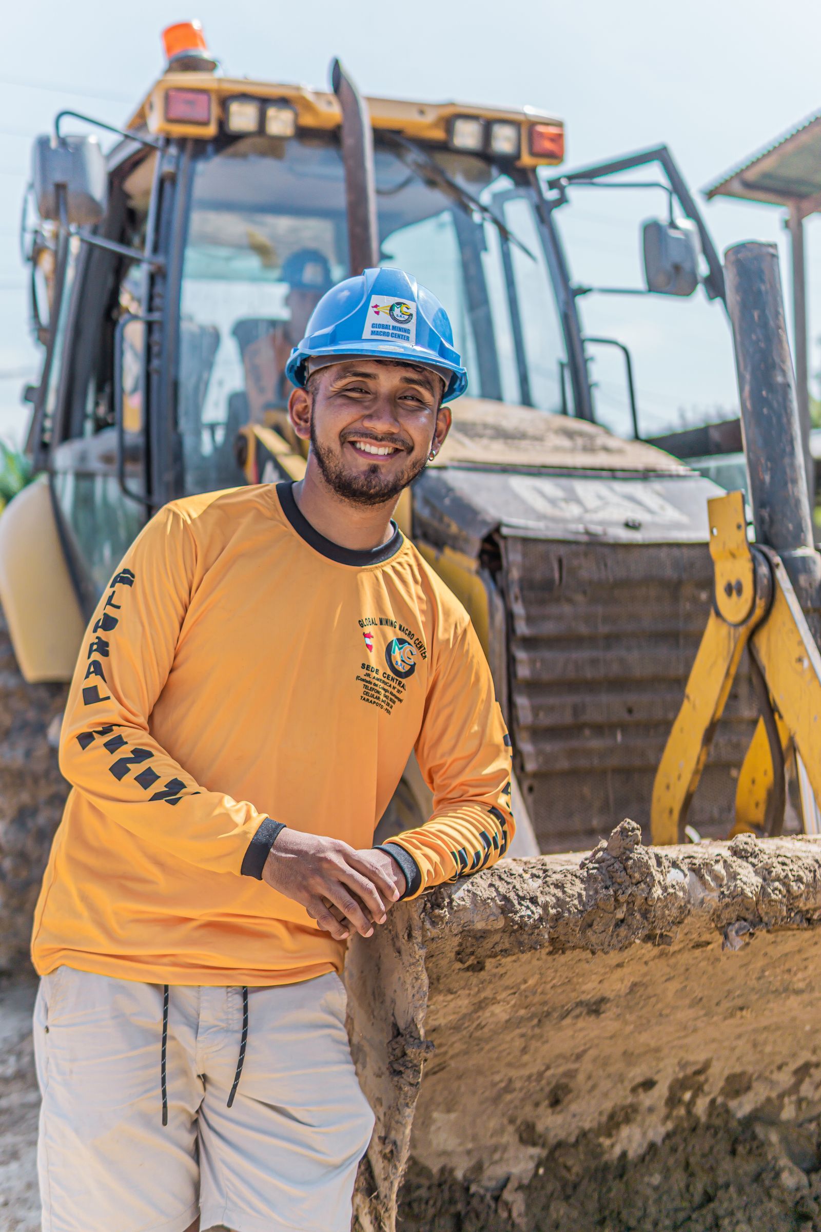 Smiling construction worker poses beside a bulldozer on a sunny day.